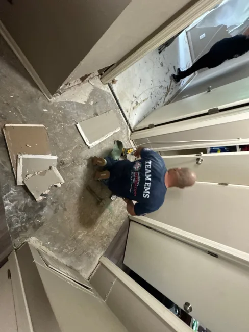 EMS technician removing flood-damaged drywall during apartment water mitigation