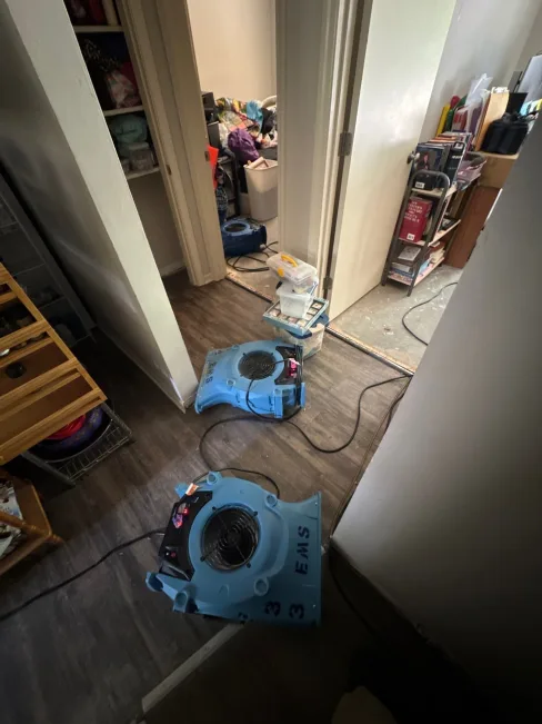 Air movers and dehumidifiers running in an apartment laundry room during flood mitigation